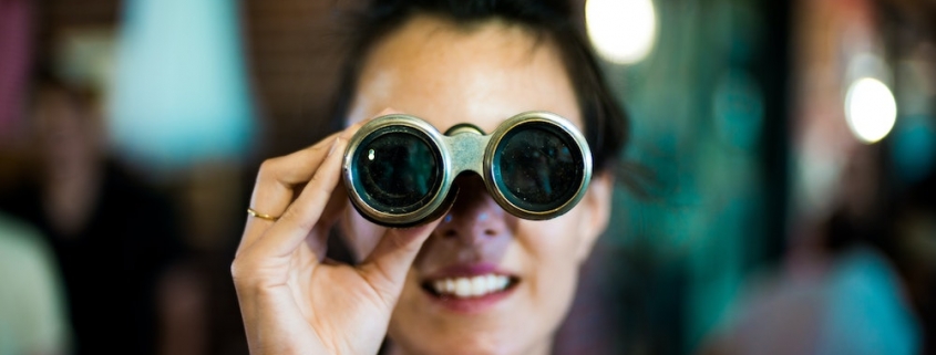 Blog header image showing a woman with binoculars for the Solver blog on how to use monthly rolling forecasts to gain insight in unpredictable times